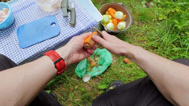 POV male hands peeling a raw carrot with peeler at an outdoor camping picnic
