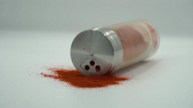 Spilled Red Spice Powder from a Glass Shaker Isolated on White