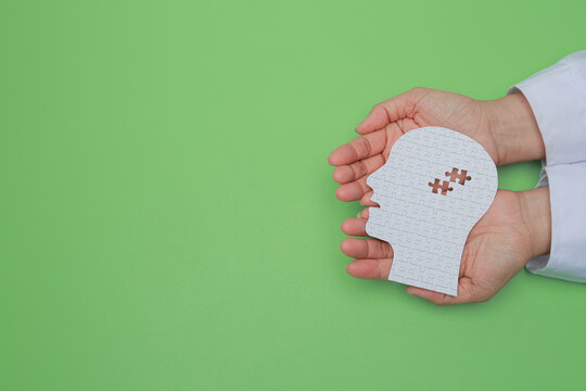 Doctor hand holding paper head with brain puzzle offering compassionate mental health care and psychology support on green background