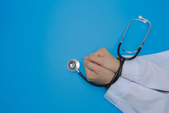 Stressed doctor hand tied with stethoscope in white lab coat showing medical integrity and heavy professional pressure on blue background
