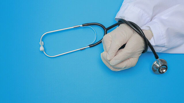 Doctor wearing white glove with hand tied by stethoscope on blue background conveys stressed emotion while upholding medical integrity