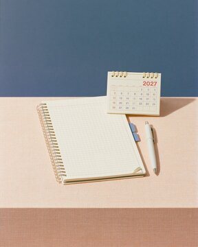 Spiral notebook with a small 2027 desk calendar and pen, featuring a clean and organized flat-lay for business scheduling and annual planning