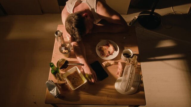 Caucasian young adult man lying passed out on table among empty beer cans and bottles in top view. Clip useful for addiction recovery campaigns, mental health awareness, substance abuse PSA