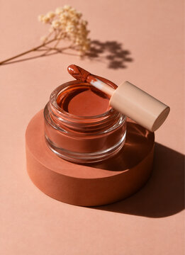 Terracotta liquid blush jar with applicator on pedestal.
