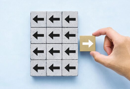 A person placing a gold block with a right arrow icon against a grid of grey blocks pointing left for business disruption and innovation concept