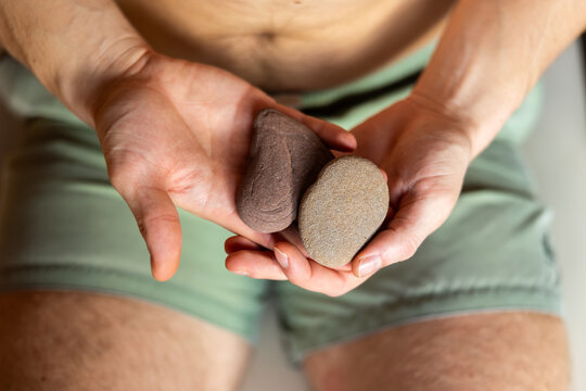 Man in swim trunks holding two hot stones used for spa treatments