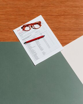 Reading glasses and a red pen resting on a printed audit sheet, set on a polished oak desk with ample copy space for business paperwork