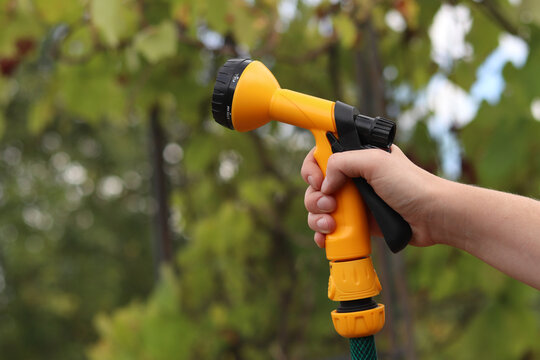 Garden spray gun for watering in hand on blurred green background, garden care, watering plants, spring-summer garden work. A woman's hand holds a bright yellow plastic spray gun for watering