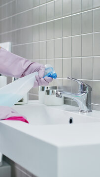 Close up of hands wearing rubber gloves spraying detergent and wiping chrome faucet with cloth