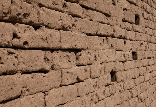 A detailed close-up of a weathered, rustic adobe mud brick wall texture for background