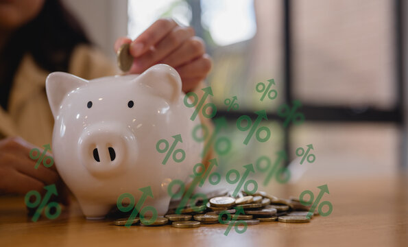 Saving money and financial planning concept. Woman hand putting coin in to piggy bank on wood table, income, return, retirement, compensation fund, investment, dividend tax, stock market