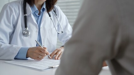 Doctor taking notes during medical consultation with patient, discussing healthcare information and...
