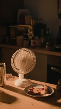 Vertical shot of small desk fan rotating beside leftover food and beverage can on kitchen table. Footage suitable for projects about alcoholism, loneliness, or depression