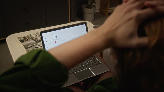 Rear view of young man watching bank balance drop to zero on laptop screen, grabbing head in shock. Clip fits themes of cyber fraud, crypto crash, bankruptcy, and personal financial crisis