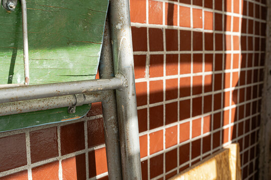 Metal construction frame and green wooden plank against brown tile wall with hard shadows