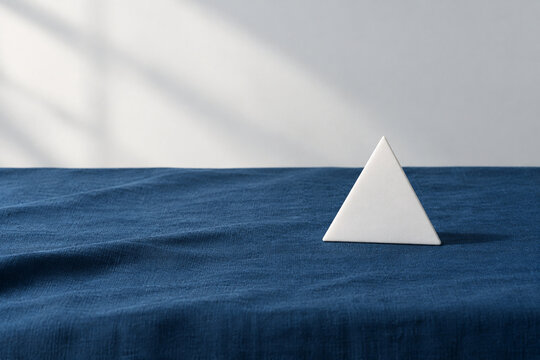 Single white equilateral triangle object on deep blue linen, calm still life for editorial concept