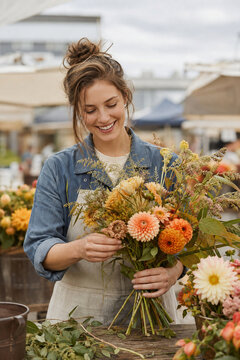 Smiling florist arranging a seasonal flower bouquet at outdoor market