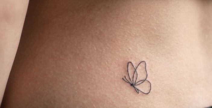 Macro Close Up of Delicate Fine Line Butterfly Tattoo on Woman Lower Back and Waist