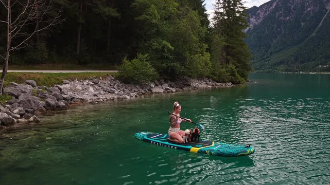 A woman paddleboards with dogs on Lake Achensee in Tyrol, Austria - drone shot