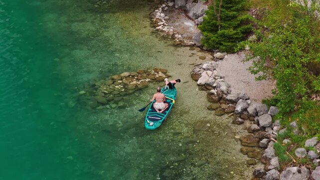 A woman paddleboards near the rocky shore of Lake Achensee in Tyrol, Austria, with clear lake water and rocky shoreline visible - drone shot
