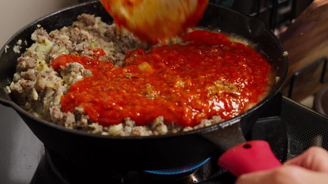 Adding tomato sauce to ground beef and onions in a cast iron skillet
