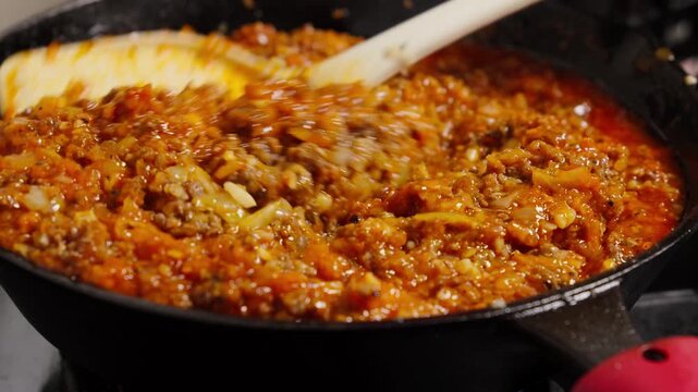 stirring hot and steaming bolognese sauce in pan, cooking bolonese sauce