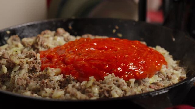 Adding tomato sauce to ground beef and onions in a cast iron skillet