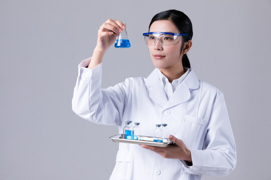 Scientist holding Erlenmeyer flask with blue liquid on tray of vials