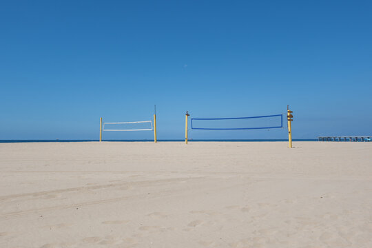 Empty beach volleyball nets set up on clean sand facing the vast blue ocean and sky in Hermosa Beach, California.