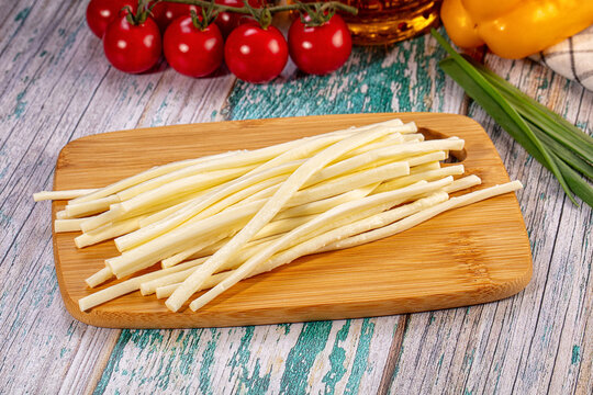 String cheese sticks piled on wooden cutting board with cherry tomatoes and yellow bell pepper in background on rustic painted wood surface