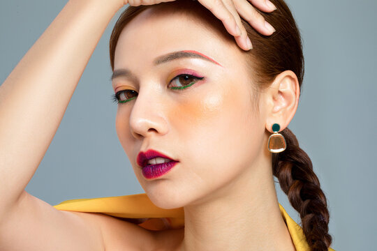 Woman with colorful eye makeup and braided hair posing in studio
