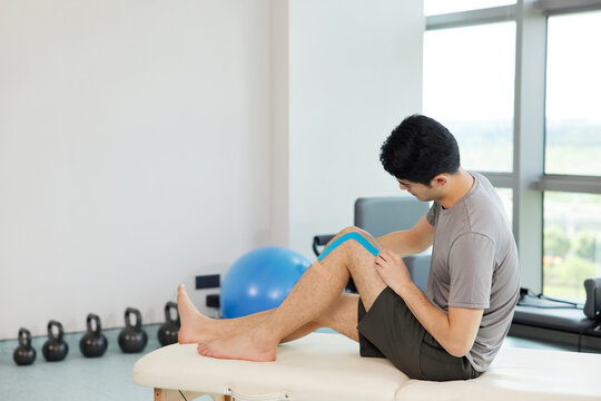 Man Applying Kinesiology Tape to Knee in Fitness Studio