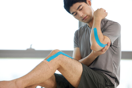 Man grimacing with arm and knee pain, blue tape on arm and knee