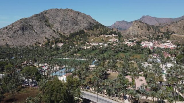 Smooth drone video zooming in on the lush Orihuela palm grove and San Anton district in Alicante, Spain. High-quality stock footage of European nature and city architecture.
