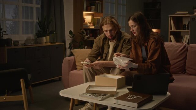 Young Caucasian couple unboxing damaged parcel and photographing product using smartphone. Footage useful for ecommerce return policy, customer service or delivery complaint visuals