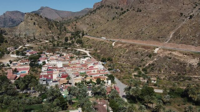 Drone shot flying parallel to San Ant&oacute;n neighborhood in Orihuela, Spain, revealing the N-340 highway with scenic mountain views and urban traffic.