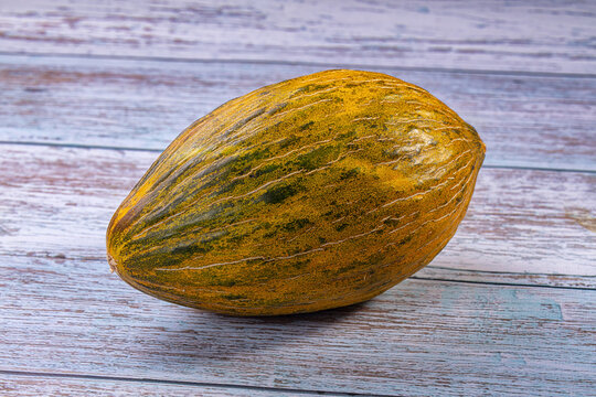 Ripe piel de sapo melon with yellow and green striped rind resting on weathered blue wooden surface