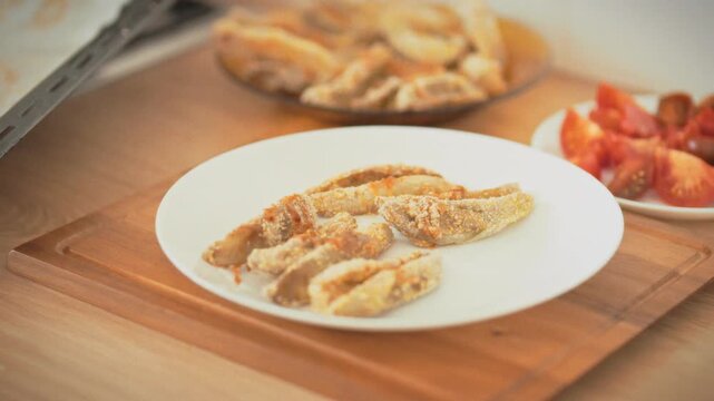 A housewife plates oven-baked eggplant from a baking tray onto a white dish using tongs in a home kitchen. Healthy baked food made by hand. Theme of homemade natural cooking