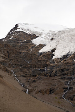 Glacier cap with meltwater streams trickling down rugged mountain rock face in Tibet