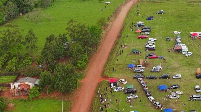 Rally car racing past roadside camps in Nueva Alborada countryside, Paraguay, aerial dolly descend