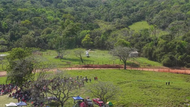 Rally spectators gathered beside a dirt course in Nueva Alborada, Paraguay, aerial approach to helicopter in field
