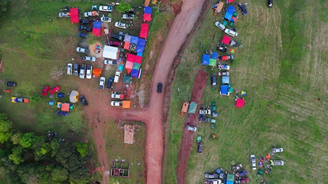 Rally campsite with tents and parked cars along dirt roads in Nueva Alborada, Paraguay, aerial tracking follows pace car on road