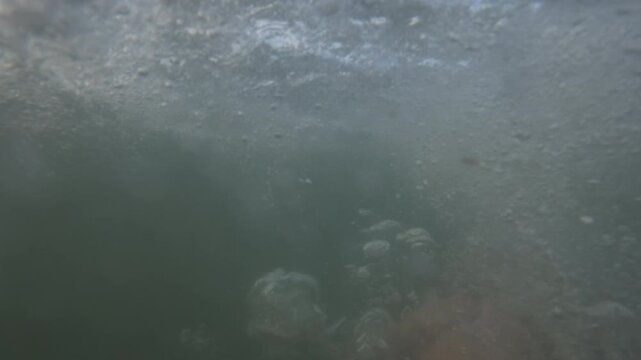 Underwater close-up of bubbles and barnacle-covered rocks near the choppy surface, Golfe-Juan, France
