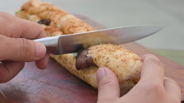 Close-up slow motion hands slicing a fresh long submarine sandwich in half with a kitchen knife on a wooden cutting board, horizontal