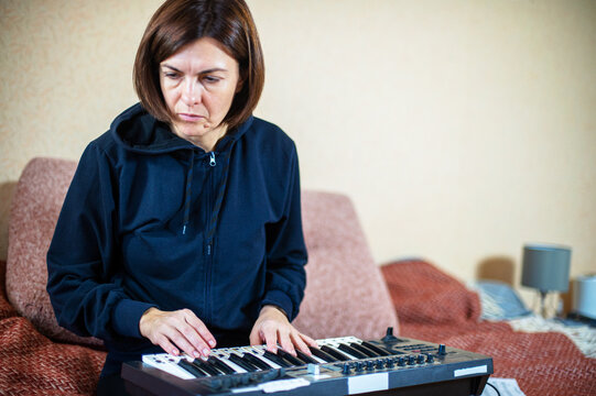 Woman playing electronic keyboard synthesizer at home in a casual black hoodie