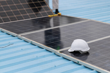 Close-up of solar panels being installed on a blue metal roof, with a white safety helmet resting...