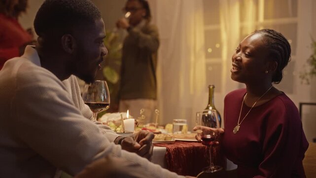African American young adult man and woman drinking wine and talking at holiday dinner. Perfect for Thanksgiving promotional campaigns and lifestyle advertisements