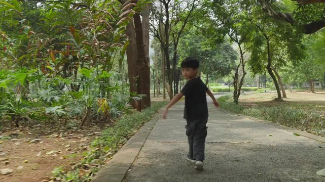 rear view of a young child walking along a paved path through a tree lined park