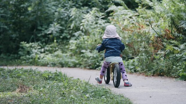 Unrecognizable young girl is riding a bicycle down a path in a forest. The scene is peaceful and serene, with the girl enjoying her ride and the natural surroundings, slow motion
