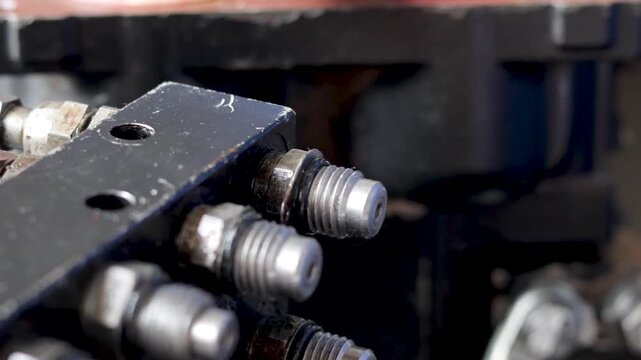 Static shot of mechanic installing threaded hydraulic fitting onto manifold block in workshop.